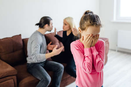 Frustrated little girl feeling depressed while angry parents fighting at home. Worried upset small daughter hurt by fathers and mothers break up or divorce, children and family conflict concept.の写真素材