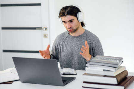 male teacher wearing wireless headphones, holding online lesson looking at laptop. Millennial pleasant professional man tutor giving online language class. Distant learningの写真素材