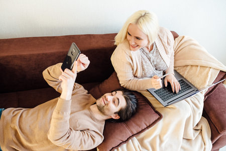 Beautiful couple, young man and blonde woman doing an online payment from the comfort of her living...