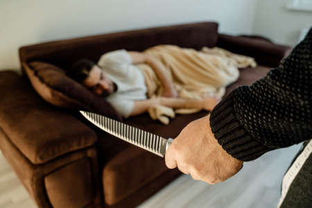 Crime Concept. human hands with knife ready to attack man who is sleeping in bed at home in the middle of the nightの写真素材