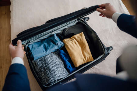 From above anonymous male in suit packing clothes and closing suitcase on bed while preparing for business trip at homeの写真素材