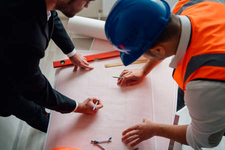 From above crop businessman and contractor drawing draft on table while working on architectural project in office togetherの写真素材