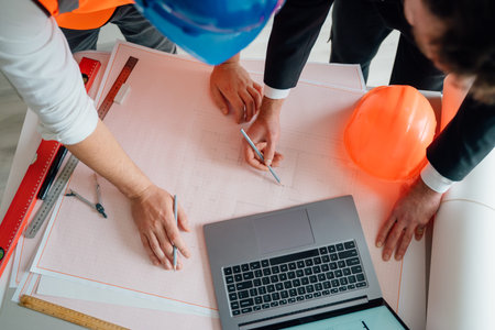 top view of workers pointing to building on blueprint and using laptop to drawing design building Project in office, construction concept.の写真素材