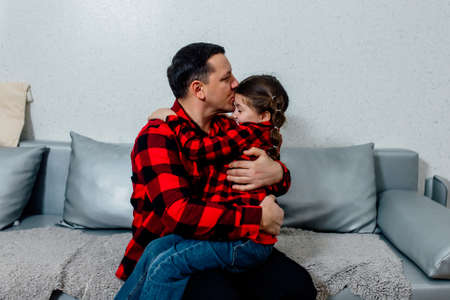 father hugs his daughter and kisses her on the forehead. happy father sitting on the couch at home hugging his daughter. paternityの写真素材