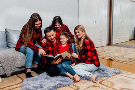 Young parents read the book to children at home. happy loving family. pretty young father reading a book to her daughtersの写真素材
