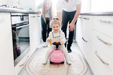 american parents having fun with little daughter on the pink car in the kitchen by the window at home. traditional family with one childの写真素材