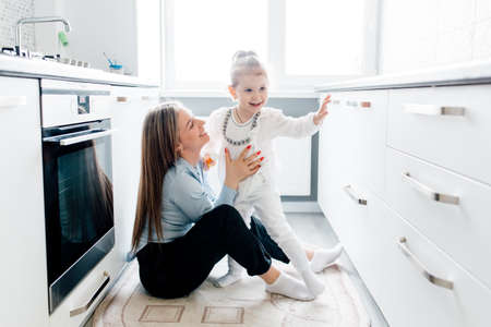 Loving young american mother laughing embracing smiling cute funny kid daughter enjoying time together at the kitchen, happy family single mom with little child girl having fun playing feel joy cuddling and huggingの写真素材