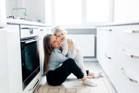 Happy caucasian mother with little daughter playing at the kitchen. happy mother and little child girl hugging having fun playing enjoy funny moments good time together.の写真素材