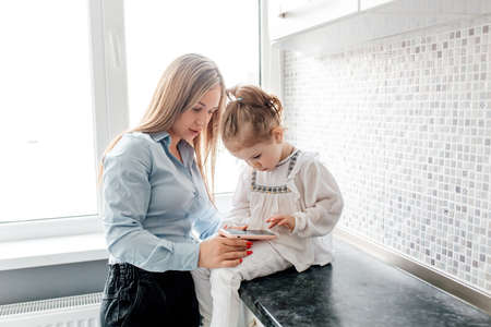 mom's Love, mother's day. mother and his daughter child girl playing with smartphone at the kitchen together near window, At Home. Parenting And motherhood Joy Conceptの写真素材