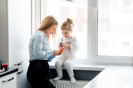 loving single mother holding cute little child daughter playing at home. they have fun together at home in the kitchen by the windowの写真素材