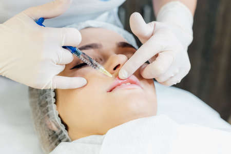 Close up of cosmetic injection in female lips. top view of cosmetologist using syringe with special liquid and holding patients chin, Concept of cosmetology, beauty.の写真素材
