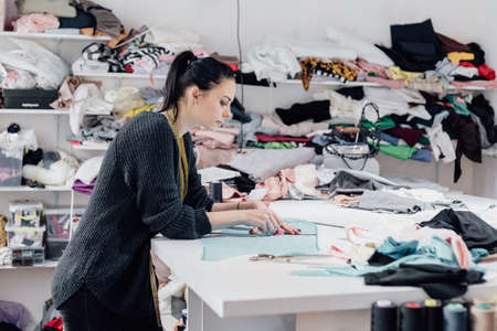 Fashionable business seamstress, portrait of happy woman tailor workplace sews. woman tailor in the workshop takes measuresの写真素材