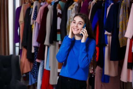 beautiful young girl with a beautiful smile speaks on the phone, she is advised, Beautiful girl front of modern clothes wardrobe closet in the shopping store. shopping, fashion, style and people conceptの写真素材