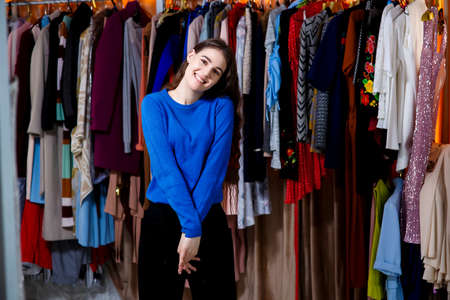 beautiful brunette teen with hands posing, looking at camera. Beautiful young woman near rack near hangers with clothing. shopping, fashion, style and people conceptの写真素材