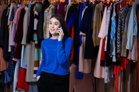 inspired teenage girl in blue sweater talking on the phone, Beautiful girl front of modern clothes wardrobe closet in the shopping store. shopping, fashion, style and people conceptの写真素材