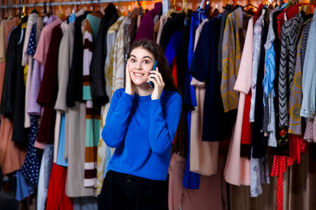 inspired teenage girl in blue sweater talking on the phone, Beautiful girl front of modern clothes wardrobe closet in the shopping store. shopping, fashion, style and people conceptの写真素材