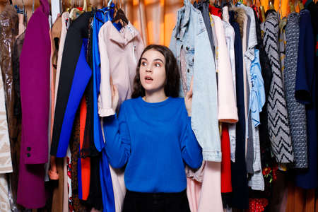 teenage girl in clothing store, amazed scared, confused. Beautiful young woman near rack near hangers with clothing. shopping store, clothing storeの写真素材