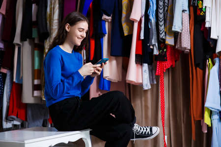 portrait of a young stylish teenager woman using a smartphone device, Beautiful girl front of modern clothes wardrobe closet in the shopping store. shopping, fashion, style and people conceptの写真素材