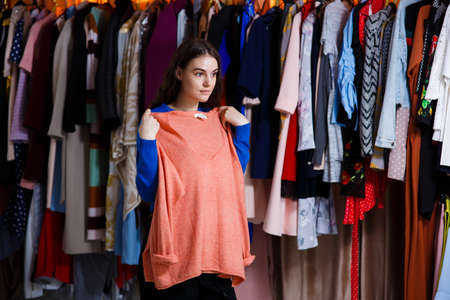 shopping, fashion, style and people concept - teen choosing clothes and looking to mirror in mall or clothing store. sale, consumerism, fashion, communication and people conceptの写真素材