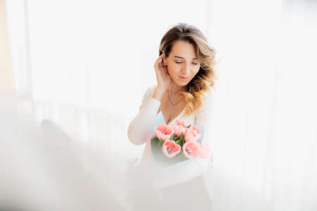 beautiful woman with a bouquet of flowers in her hands. tulip flowers in the hands of a Caucasian woman. spring time. near the windowの写真素材