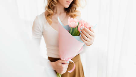 close up. Happy woman with pink flowers tulips. Beautiful young woman with spring pink flowers on the white background in the morningの写真素材