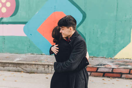 Side view of affectionate young man and woman embracing each other while having romantic date near wall with colorful painting on city streetの写真素材