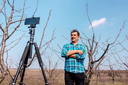 Senior farmer leads a vlog in the orchard, modern farmer using social media for marketing. Pruning fruit tree in spring.の写真素材