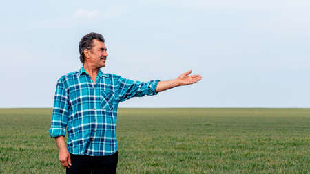 Experienced and confident farmer stands on his field with hand outstretched. Portrait of senior farmer agronomist in wheat field looking in the distance, copy spaceの写真素材