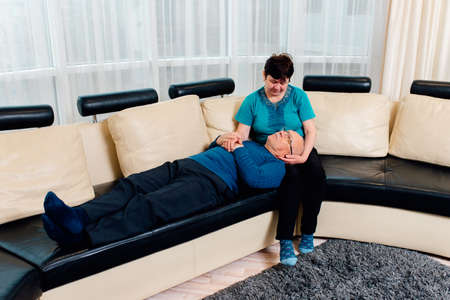 Smiling mature wife lying husband on knees, relaxing at home, happy aged family enjoying romantic moment, Mature couple relaxing in sofa, peaceful scene.の写真素材
