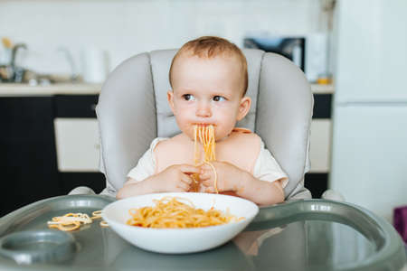 Funny toddler child with home made pasta and tomato sauce. 1 years old caucasian race boy eating spaghetti in the kitchen at home.の写真素材