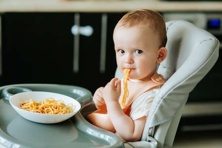 home in the kitchen little boy boy eating spaghetti pasta with red sauce. baby boy eating appetizing pasta aloneの写真素材