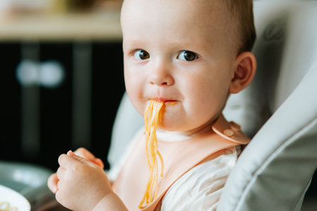 close up. home in the kitchen little boy boy eating spaghetti pasta with red sauce. baby boy eating appetizing pasta alone.の写真素材