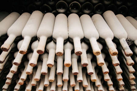 A lot of old wine bottles covered with dust. Resting wine bottles stacked on wooden racks in cellarの写真素材