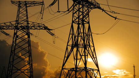 Electricity poles and electric power transmission lines against vibrant orange sky at sunset. Silhouette of power lines and stations with orange cloudy skyの写真素材