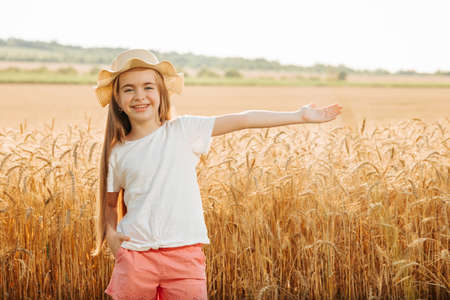 Portrait of smiling kid with hat standing in wheat field with his arms outstretched. looking at camera,の写真素材