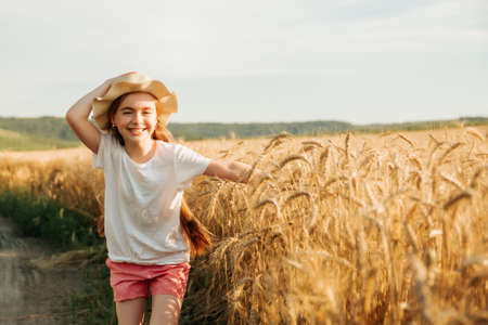 adorable little girl runs happily on the road near the yellow wheat field. child with a way of life and a happy childhood.の写真素材