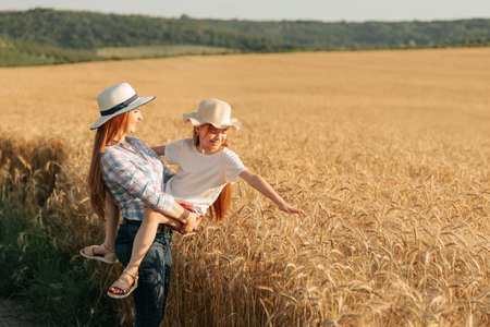 woman farmer with hat holds her child in her arms. woman and child in the golden wheat field. family of farmers happy daughter and mother harvest timeの写真素材