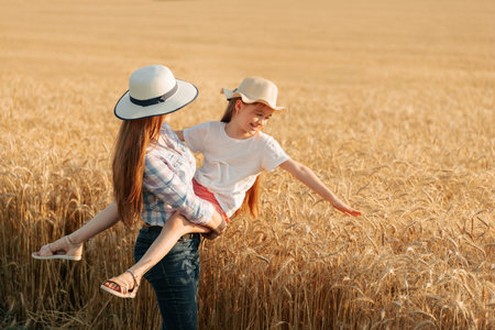 woman farmer with hat holds her child in her arms. woman and child in the golden wheat field. family of farmers happy daughter and mother harvest timeの写真素材