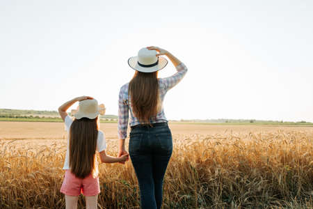 Rear view of family farmer woman and child with hat on golden wheat field at sunsetの写真素材
