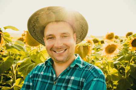 portrait of farmer in a sunflower field and looking at camera. young farmer man is standing and smiling in a sunflower field. Agriculture and nature concept.の写真素材