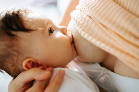 Mother feeding baby at home. Breastfeeding mother with little child. Young woman nursing and feeding baby. Concept of lactation infant.の写真素材