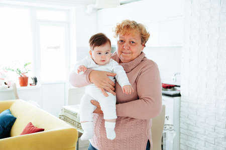 elderly woman holding her baby granddaughter kiss at home young and old people together. Adorable little kid smiling and laughing with Senior woman. Family having fun.の写真素材