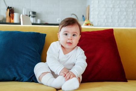 cute baby sitting on colorful sofa in living room.の写真素材