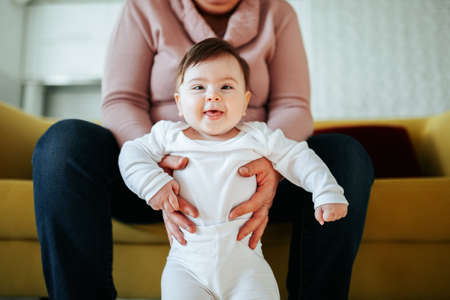 Grandmother with her cute granddaughter baby, smiling, talking, playing. Happy relaxed older adult granny embracing preschool child granddaughter cuddling bonding rest on couch at home.の写真素材
