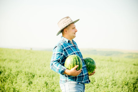 profile view of a farmer man with a watermelon in his arms, man with a hat dressed in a blue shirt with squaresの写真素材