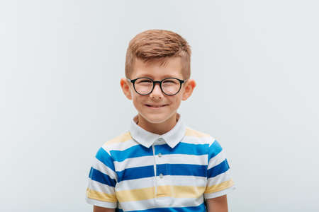 the portrait of a cheerful boy with glasses smiles in front of the camera. kid looking at camera is happy. studio footage on the white backgroundの写真素材