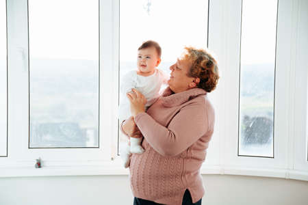 elderly woman holding her baby granddaughter kiss at home young and old people together. Adorable little kid smiling and laughing with Senior woman. Family having fun.の写真素材