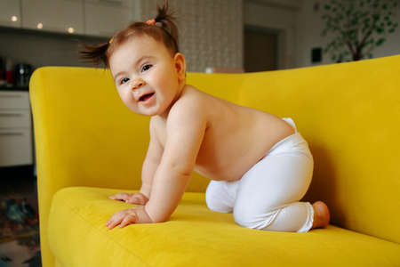 Cute Little Baby Girl on the yellow Sofa Making First Steps At Home. Happy Toddlers Portrait. Joy Of Childhood, Parenthood And Child Care Concept.の写真素材