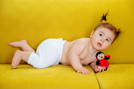 cute baby girl, on the yellow sofa at home in the living room and looking at camera. beautiful childrenの写真素材