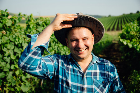 cheerful man with modern young winemaker hat is on the vineyard. the portrait of the winemaker looking at the cameraの写真素材